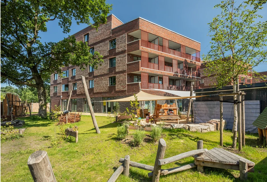 Kita-Gebäude mit naturnahem Spielplatz im Garten bei Sonnenschein