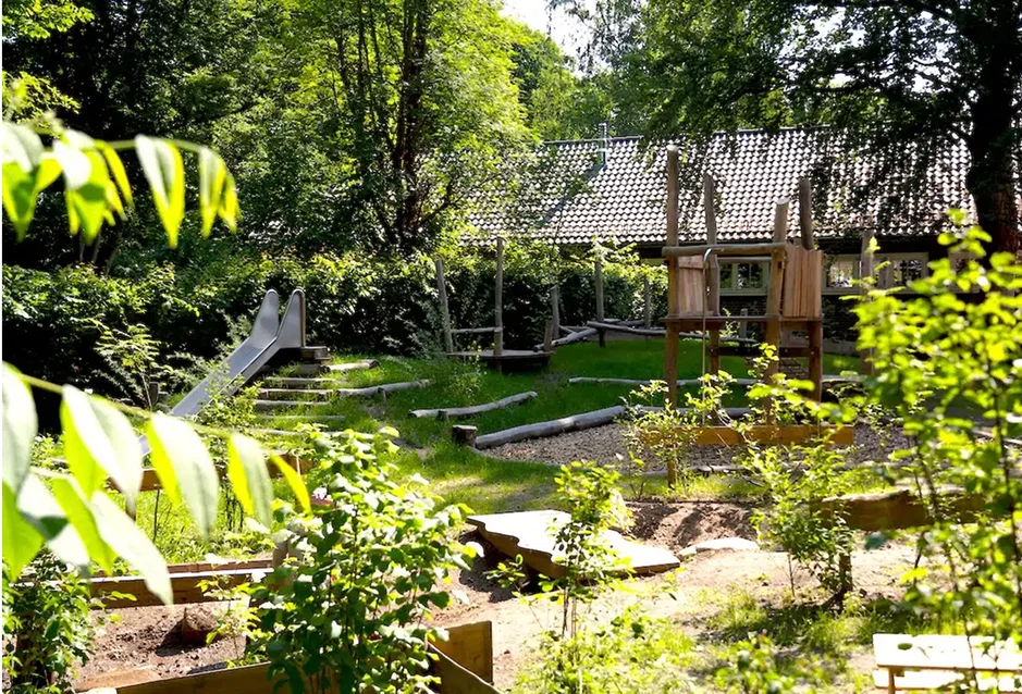 Grüner Kita-Garten mit Holzspielgeräten, Rutsche und Hochbeeten