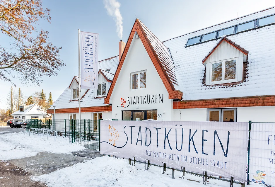 Verschneites Gebäude der Kita Stadtküken mit Banner und Flagge im Außenbereich