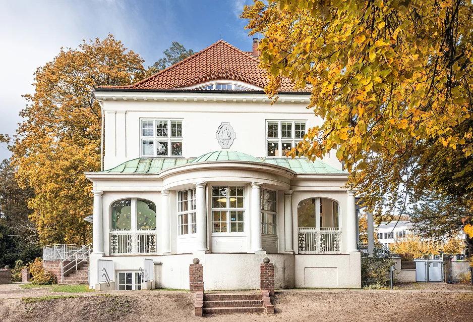 Weiße Jugendstilvilla mit rotem Dach und herbstlicher Baumkulisse