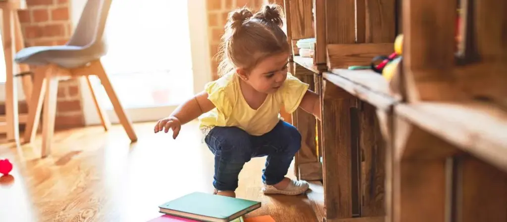 Kleines Mädchen stöbert neugierig in einem Holzregal mit Büchern