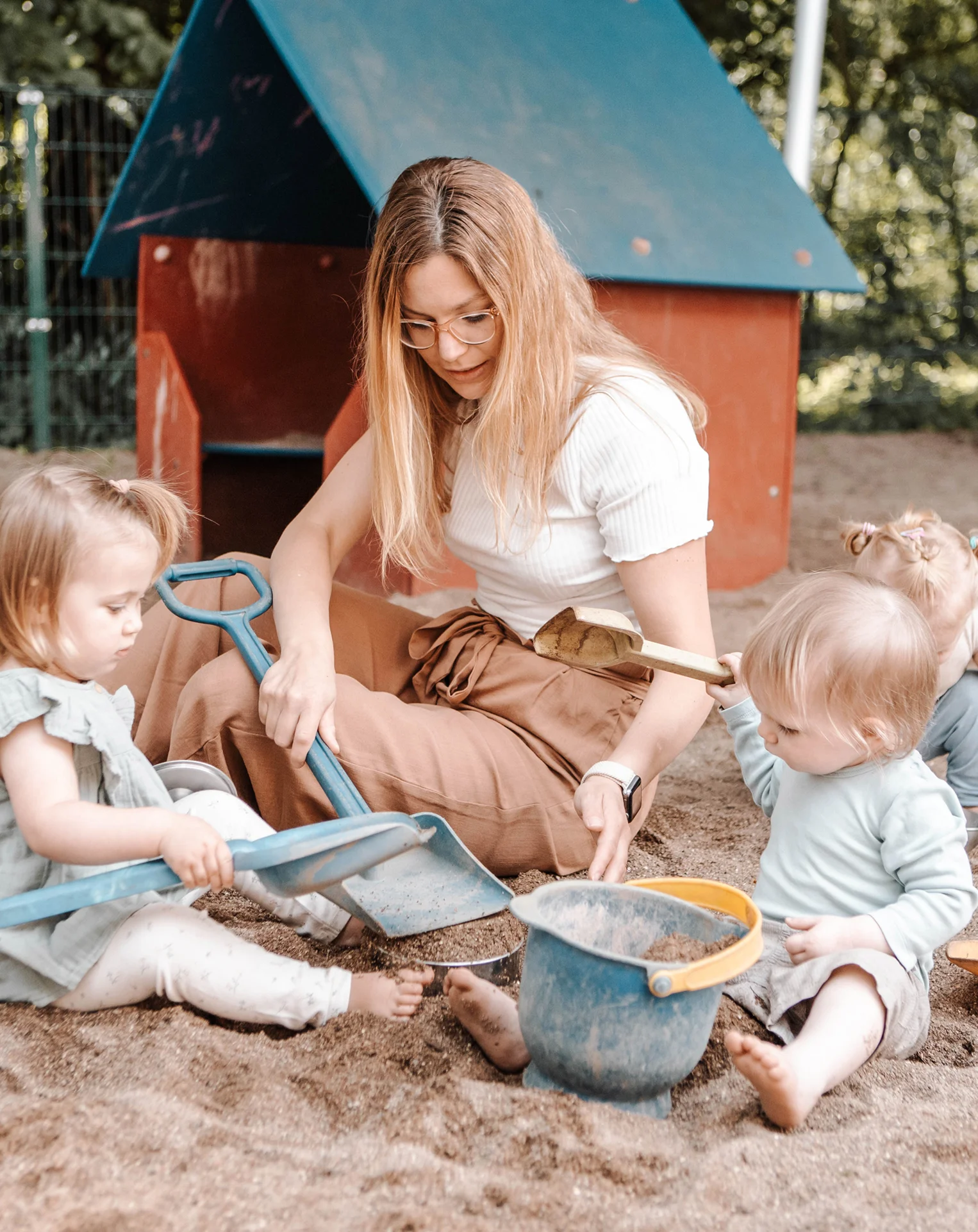 Erzieherin spielt mit Kleinkindern im Sandkasten