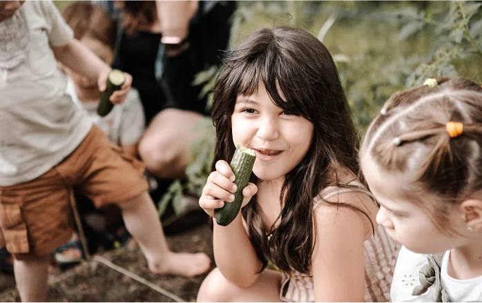 Kind beißt lachend in eine frisch geerntete Gurke im Garten