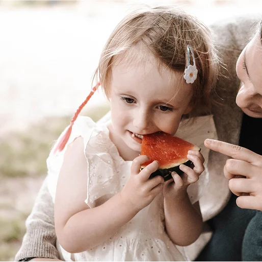 Kleines Mädchen isst ein Stück Wassermelone mit Freude
